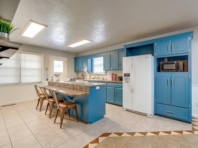 825 W 22nd St, Ada, OK 74820 - kitchen with white fridge with ice dispenser, blue cabinetry, black microwave, a kitchen breakfast bar, and a textured ceiling