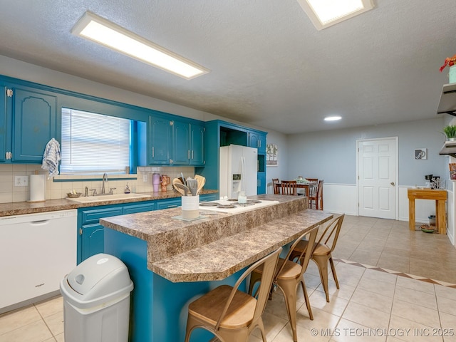 825 W 22nd St, Ada, OK 74820 - kitchen with white appliances, blue cabinetry, a center island, light tile patterned floors, and a kitchen bar
