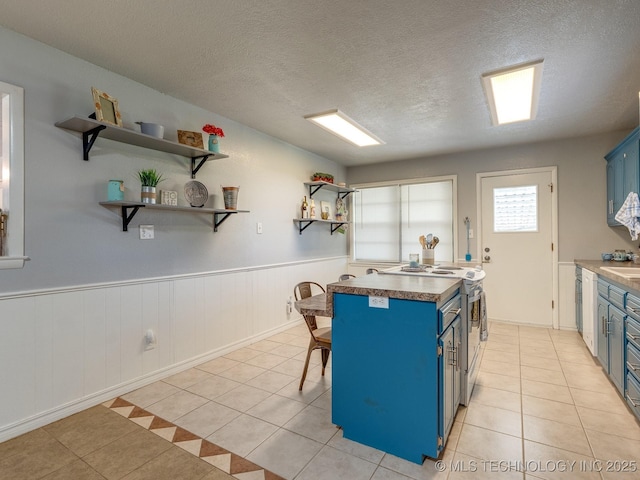 825 W 22nd St, Ada, OK 74820 - kitchen featuring blue cabinets, light tile patterned floors, open shelves, white stove, and wainscoting