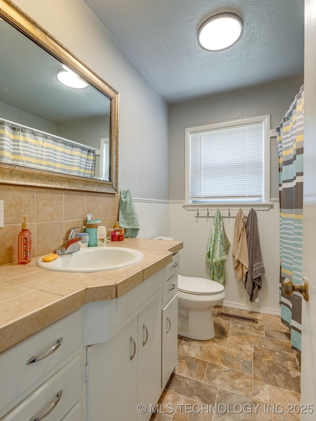 825 W 22nd St, Ada, OK 74820 - full bathroom featuring vanity, a textured ceiling, wainscoting, stone finish floors, and decorative backsplash