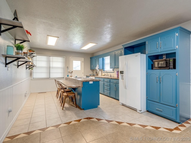 825 W 22nd St, Ada, OK 74820 - kitchen featuring blue cabinetry, white refrigerator with ice dispenser, a center island, light tile patterned floors, and a kitchen bar
