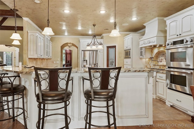 509 E Glendale St, Broken Arrow, OK 74011 - kitchen featuring appliances with stainless steel finishes, premium range hood, a peninsula, arched walkways, and crown molding