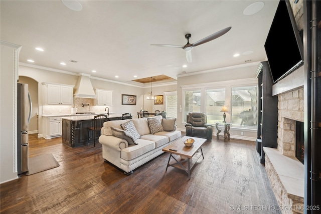 5906 E 126th Pl S, Bixby, OK 74008 - living room featuring a ceiling fan, dark wood-type flooring, crown molding, a stone fireplace, and recessed lighting