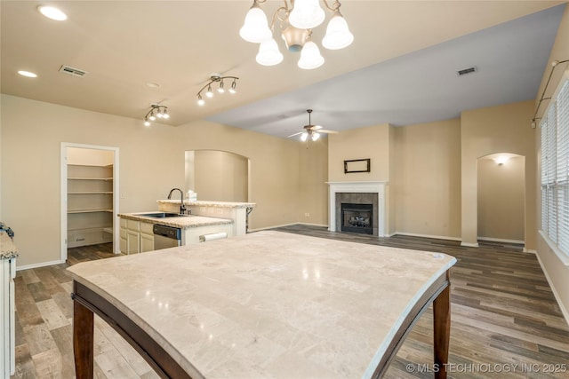 12522 S Cedar Ave, Jenks, OK 74037 - kitchen with an island with sink, a ceiling fan, arched walkways, a tiled fireplace, and dark wood-type flooring