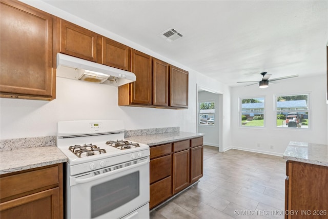 2127 W 48th Pl, Tulsa, OK 74107 - kitchen with white gas stove, under cabinet range hood, a ceiling fan, brown cabinetry, and light stone counters
