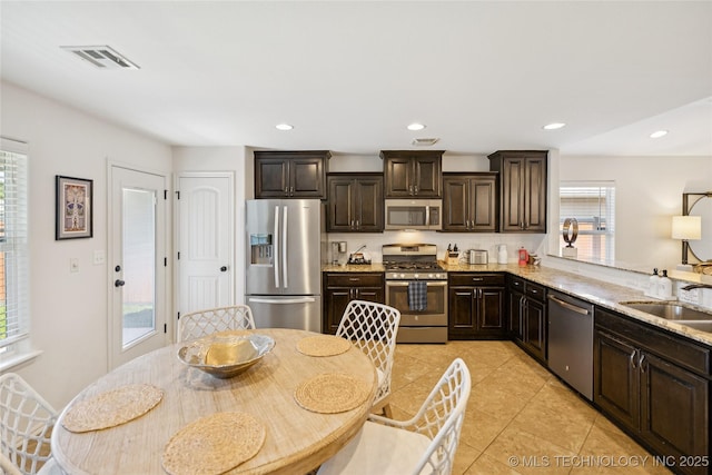 2610 E 5th Pl, Tulsa, OK 74104 - kitchen featuring appliances with stainless steel finishes, dark brown cabinets, light tile patterned floors, light stone countertops, and recessed lighting