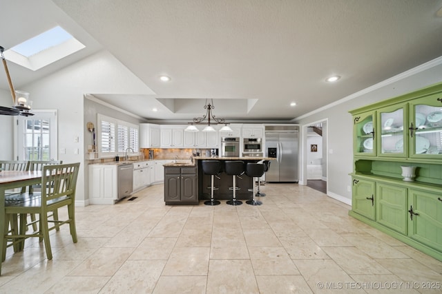 8120 E 112th St, Owasso, OK 74055 - kitchen with appliances with stainless steel finishes, a skylight, white cabinetry, ornamental molding, and a kitchen island