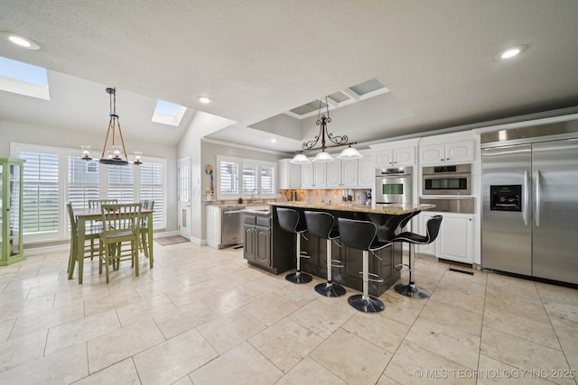 8120 E 112th St, Owasso, OK 74055 - kitchen with appliances with stainless steel finishes, a skylight, a warming drawer, white cabinetry, and a kitchen island