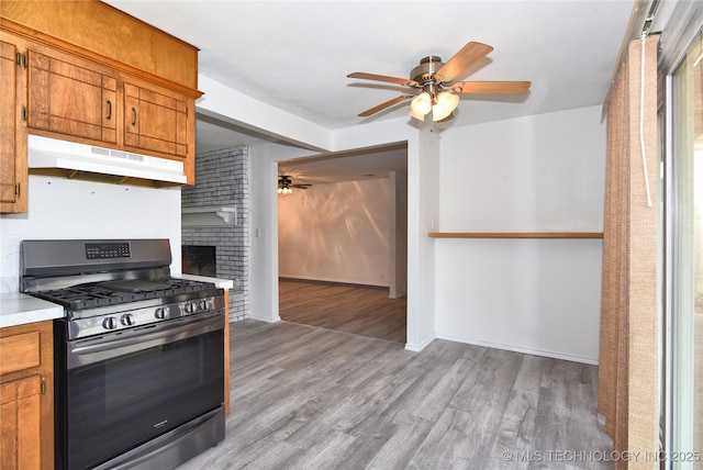 20529 E 4th St, Tulsa, OK 74108 - kitchen featuring stainless steel gas range oven, under cabinet range hood, a ceiling fan, light wood-style floors, and brown cabinetry