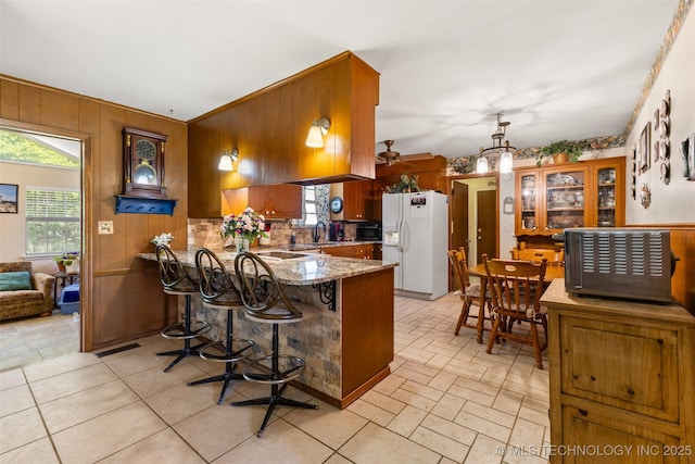 3811 Broadway Ct, Ada, OK 74820 - kitchen featuring white refrigerator with ice dispenser, a peninsula, healthy amount of natural light, light stone counters, and wooden walls
