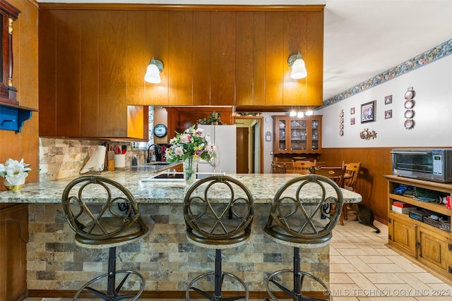 3811 Broadway Ct, Ada, OK 74820 - kitchen featuring brown cabinets, a wainscoted wall, light stone countertops, a peninsula, and freestanding refrigerator