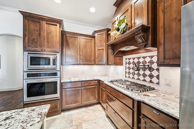 7003 E 88th St N, Owasso, OK 74055 - kitchen with stainless steel appliances, decorative backsplash, light stone countertops, arched walkways, and crown molding