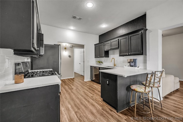 14900 E 88th St N, Owasso, OK 74055 - kitchen with a peninsula, light wood-type flooring, a kitchen bar, tasteful backsplash, and recessed lighting