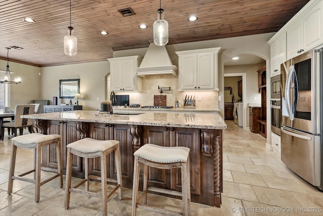10611 N 159th E Ave, Owasso, OK 74055 - kitchen featuring appliances with stainless steel finishes, custom range hood, stone tile floors, backsplash, and white cabinets