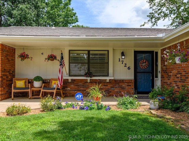 1726 Harned Dr, Bartlesville, OK 74006 - entrance to property featuring brick siding, covered porch, a yard, and a shingled roof
