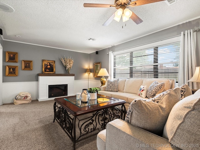 1726 Harned Dr, Bartlesville, OK 74006 - carpeted living room featuring a textured ceiling, ceiling fan, a fireplace, and a wainscoted wall