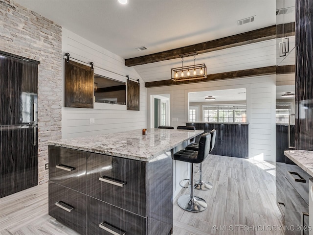 7507 S 92nd E Ave, Tulsa, OK 74133 - kitchen with a kitchen bar, beamed ceiling, light stone counters, light wood finished floors, and dark brown cabinetry