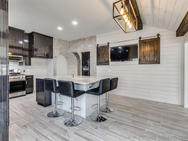 7507 S 92nd E Ave, Tulsa, OK 74133 - kitchen featuring stainless steel appliances, a barn door, a center island, light wood-style floors, and wooden walls