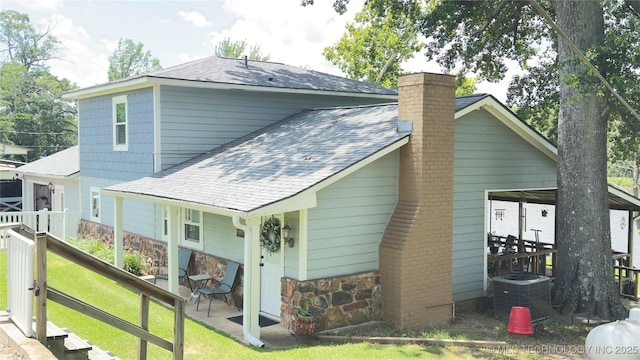 1060 Lakeside Dr, Fort Towson, OK 74735 - rear view of property featuring a shingled roof, a lawn, a chimney, and stone siding