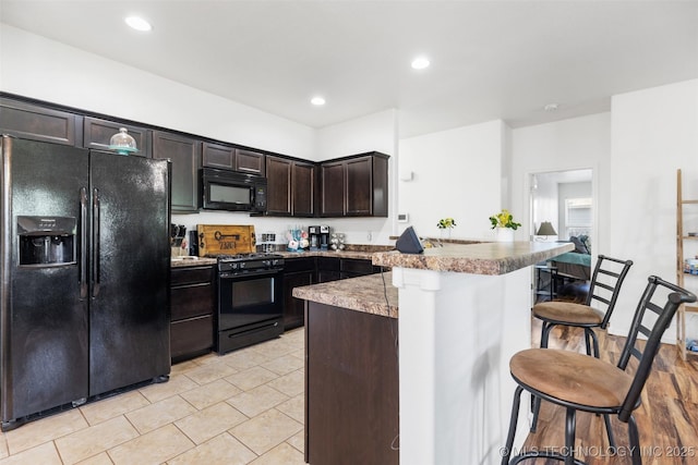 23204 S Jewell Dr, Claremore, OK 74019 - kitchen featuring black appliances, a breakfast bar, a peninsula, dark brown cabinets, and light tile patterned floors