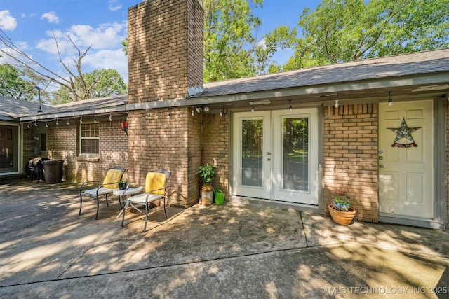 16 Big Bluff St, Pryor, OK 74361 - view of exterior entry featuring a chimney, brick siding, a patio, french doors, and a shingled roof