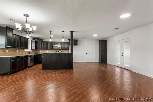 1706 S Madison Blvd, Bartlesville, OK 74006 - kitchen with appliances with stainless steel finishes, a chandelier, tasteful backsplash, dark wood finished floors, and light countertops