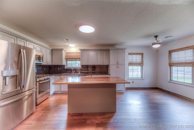 17542 W 1st St S, Sand Springs, OK 74063 - kitchen with appliances with stainless steel finishes, a kitchen island, decorative backsplash, light wood-style flooring, and a textured ceiling