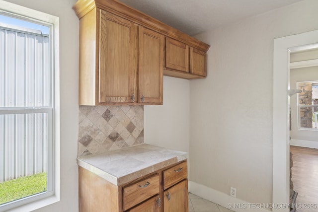 521 S Chickasaw Ave, Claremore, OK 74017 - kitchen featuring backsplash, light countertops, brown cabinetry, and healthy amount of natural light