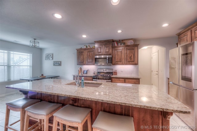 5440 Skylane Pl, Sand Springs, OK 74063 - kitchen featuring stainless steel appliances, arched walkways, light stone countertops, a kitchen breakfast bar, and backsplash
