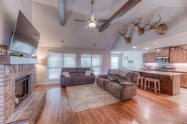 5440 Skylane Pl, Sand Springs, OK 74063 - living area featuring beam ceiling, light wood-type flooring, a brick fireplace, high vaulted ceiling, and a ceiling fan