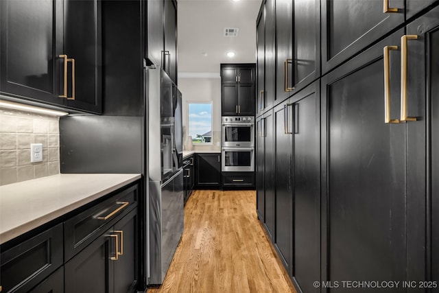17076 S 31st E Ave, Mounds, OK 74047 - kitchen featuring stainless steel appliances, dark cabinetry, light wood-style floors, tasteful backsplash, and light countertops