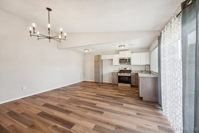 208 183rd E Ave, Tulsa, OK 74108 - kitchen with stainless steel appliances, a chandelier, vaulted ceiling, white cabinetry, and wood finished floors