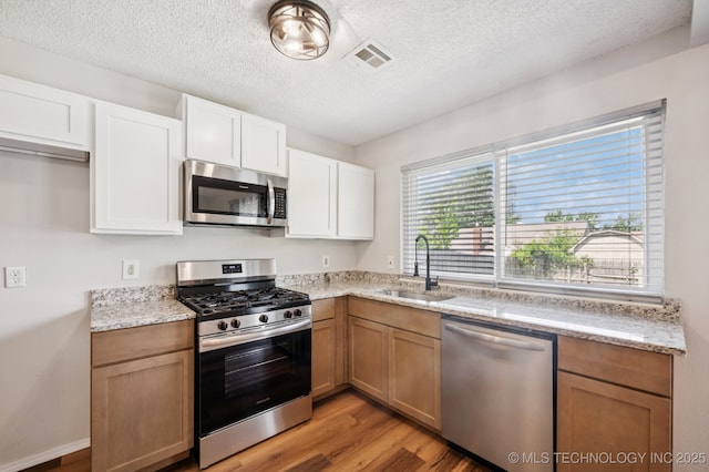 208 183rd E Ave, Tulsa, OK 74108 - kitchen with appliances with stainless steel finishes, light wood-style floors, a textured ceiling, light stone countertops, and white cabinetry