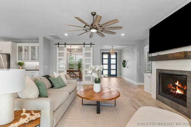 19021 E Chokeberry St, Owasso, OK 74055 - living room with a barn door, a ceiling fan, recessed lighting, light wood-style floors, and a lit fireplace