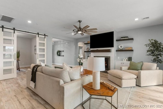 19021 E Chokeberry St, Owasso, OK 74055 - living room featuring a barn door, a ceiling fan, recessed lighting, light wood finished floors, and a warm lit fireplace