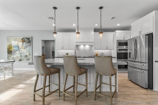 19021 E Chokeberry St, Owasso, OK 74055 - kitchen with stainless steel appliances, white cabinetry, light stone counters, a breakfast bar, and recessed lighting