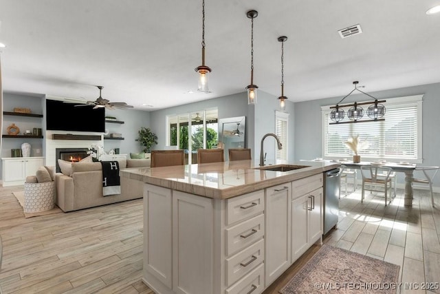 19021 E Chokeberry St, Owasso, OK 74055 - kitchen with light wood-style floors, ceiling fan, stainless steel dishwasher, a glass covered fireplace, and white cabinetry