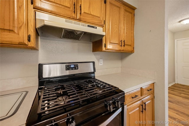 612 S 5th St, Eufaula, OK 74432 - kitchen with stainless steel range with gas stovetop, under cabinet range hood, light countertops, wood finished floors, and brown cabinetry