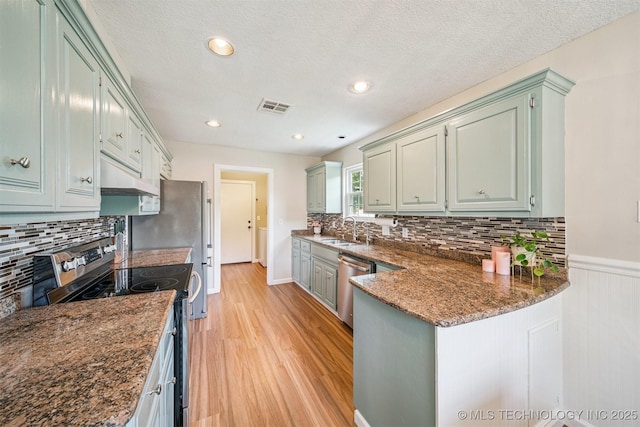 11017 E 98th St N, Owasso, OK 74055 - kitchen with stainless steel appliances, ventilation hood, light wood-style flooring, decorative backsplash, and a peninsula