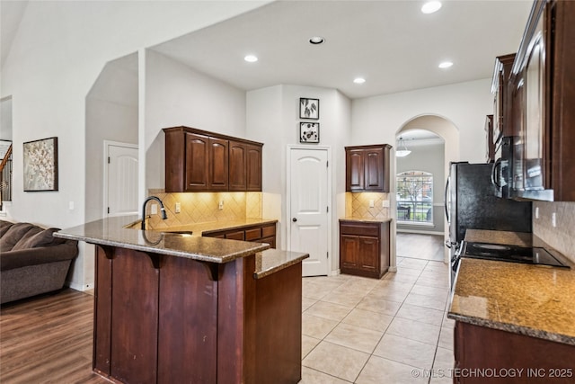 10220 N 119th E Ave, Owasso, OK 74055 - kitchen featuring arched walkways, a peninsula, dark stone countertops, a kitchen bar, and recessed lighting