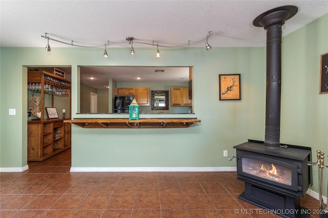 61112 E 310, Grove, OK 74344 - kitchen featuring refrigerator, a wood stove, brown cabinets, a textured ceiling, and dark tile patterned flooring