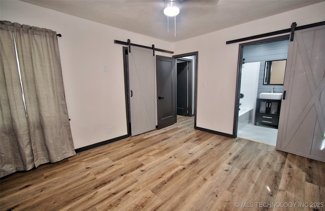 1424 E Okmulgee St, Muskogee, OK 74403 - unfurnished bedroom with a barn door, light wood-type flooring, ensuite bath, and ceiling fan