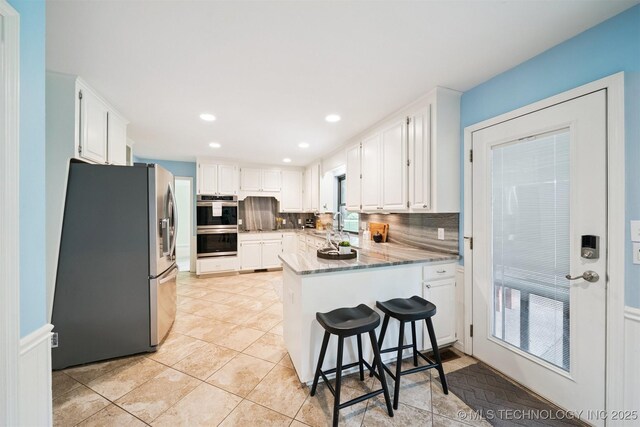 10958 S Richmond Ave, Tulsa, OK 74137 - kitchen featuring appliances with stainless steel finishes, a peninsula, decorative backsplash, white cabinets, and light stone countertops