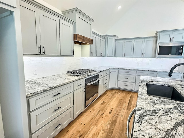 5657 E 141st Pl N, Collinsville, OK 74021 - kitchen featuring stainless steel appliances, decorative backsplash, light wood finished floors, light stone counters, and vaulted ceiling