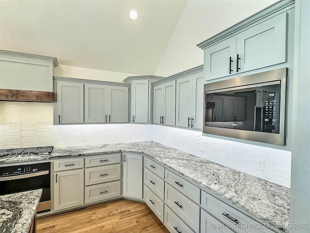 5657 E 141st Pl N, Collinsville, OK 74021 - kitchen with appliances with stainless steel finishes, vaulted ceiling, tasteful backsplash, light stone countertops, and light wood-style floors