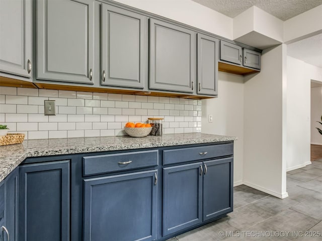 3609 Dana Dr, Bartlesville, OK 74006 - kitchen featuring blue cabinetry, backsplash, light stone countertops, a textured ceiling, and gray cabinetry