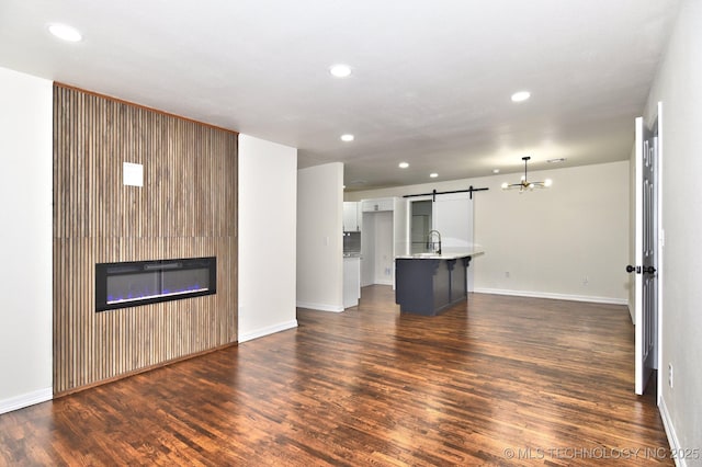 4636 E Independence St, Tulsa, OK 74115 - unfurnished living room featuring a barn door, dark wood-type flooring, recessed lighting, a glass covered fireplace, and a chandelier