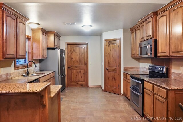 740384 S 3480th Rd, Cushing, OK 74023 - kitchen featuring stainless steel appliances, light stone counters, brown cabinets, and a peninsula