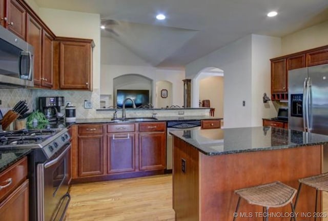 203 E 125th Pl S, Jenks, OK 74037 - kitchen with stainless steel appliances, arched walkways, light wood finished floors, a center island, and decorative backsplash