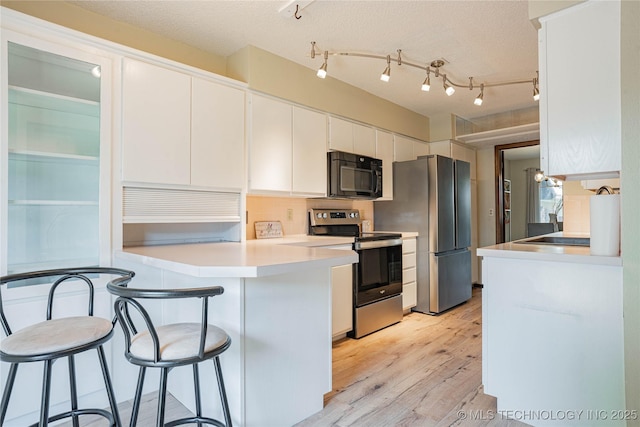 32 SE Shadowlake Dr Unit 32, Bartlesville, OK 74006 - kitchen featuring appliances with stainless steel finishes, a kitchen bar, white cabinets, a peninsula, and light wood-style floors